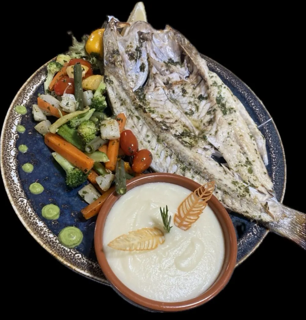 Poisson entier grillé aux herbes, légumes sautés et purée dans une cassolette en terre