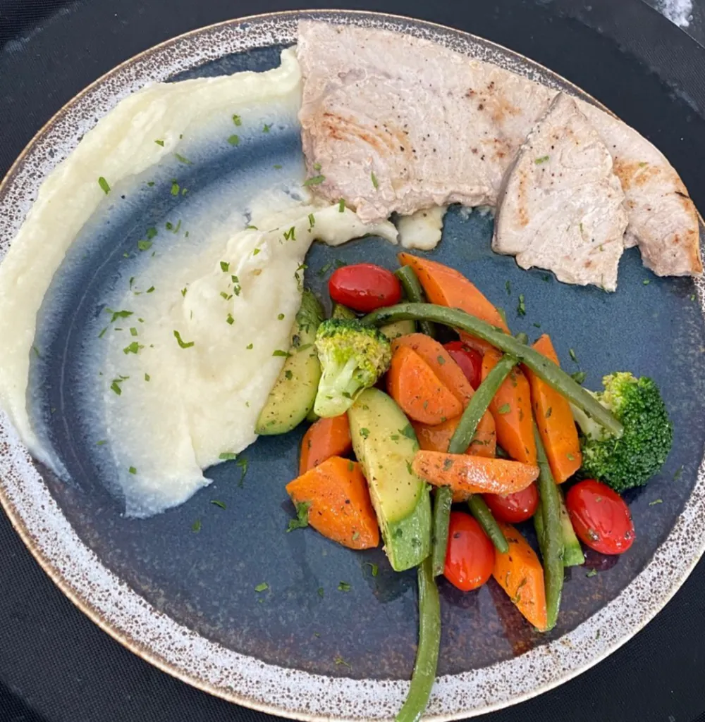 Filet de poisson grillé, purée onctueuse et légumes croquants dans une assiette bleue