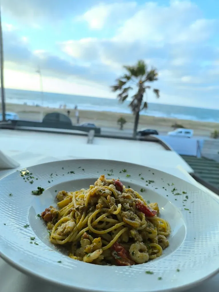 Assiette de pâtes aux crevettes et tomates, la plage d'El Jadida et un palmier en arrière-plan