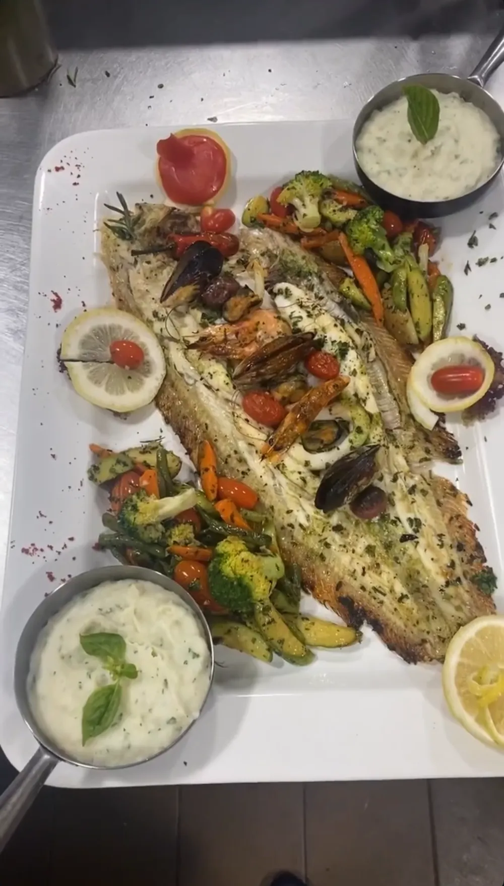 Grand plateau de poisson entier grillé aux herbes, garni de crevettes, moules et tomates cerises, avec légumes sautés, citron et deux poêlons de purée